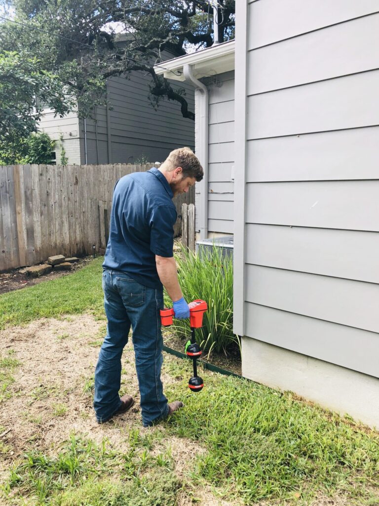Professional plumber using leak detection equipment near home foundation, assessing potential plumbing issues to prevent water damage.