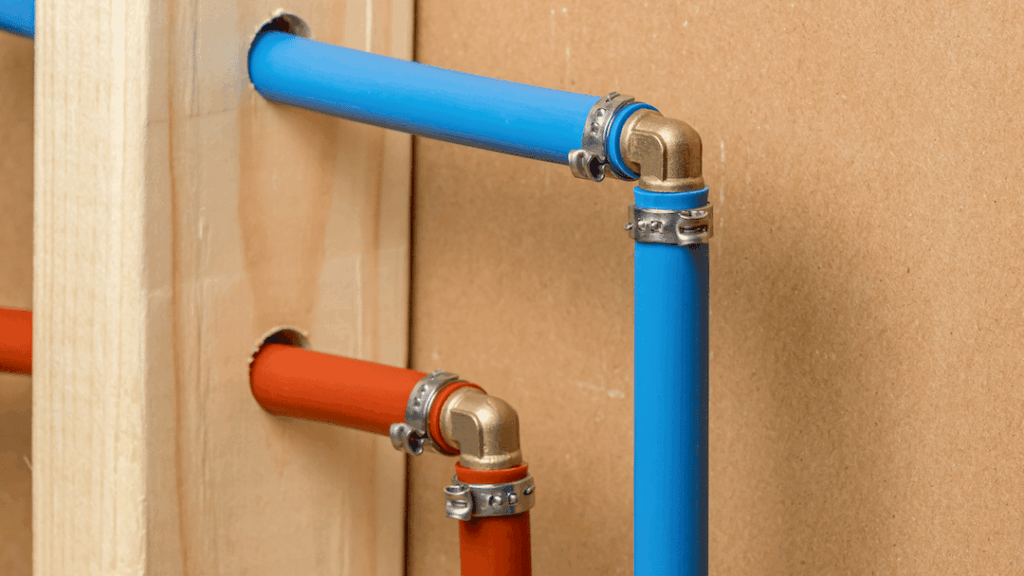 Blue and red PEX pipes with brass fittings installed on a wooden surface, illustrating modern plumbing materials used in repiping services for improved water quality and pressure.