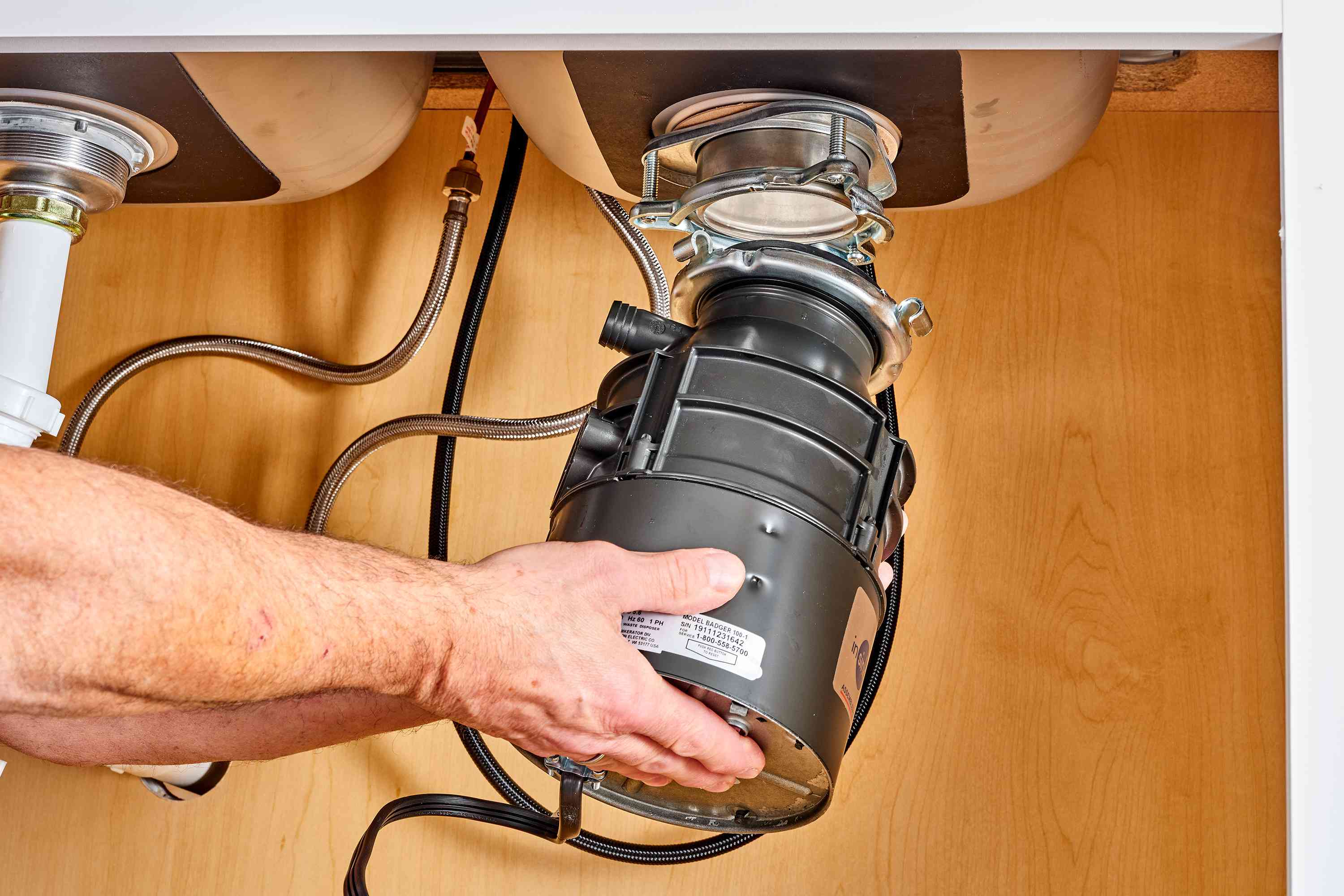 Hand installing a garbage disposal unit under a kitchen sink, showcasing plumbing connections and installation process for garbage disposal services in Pflugerville, TX.