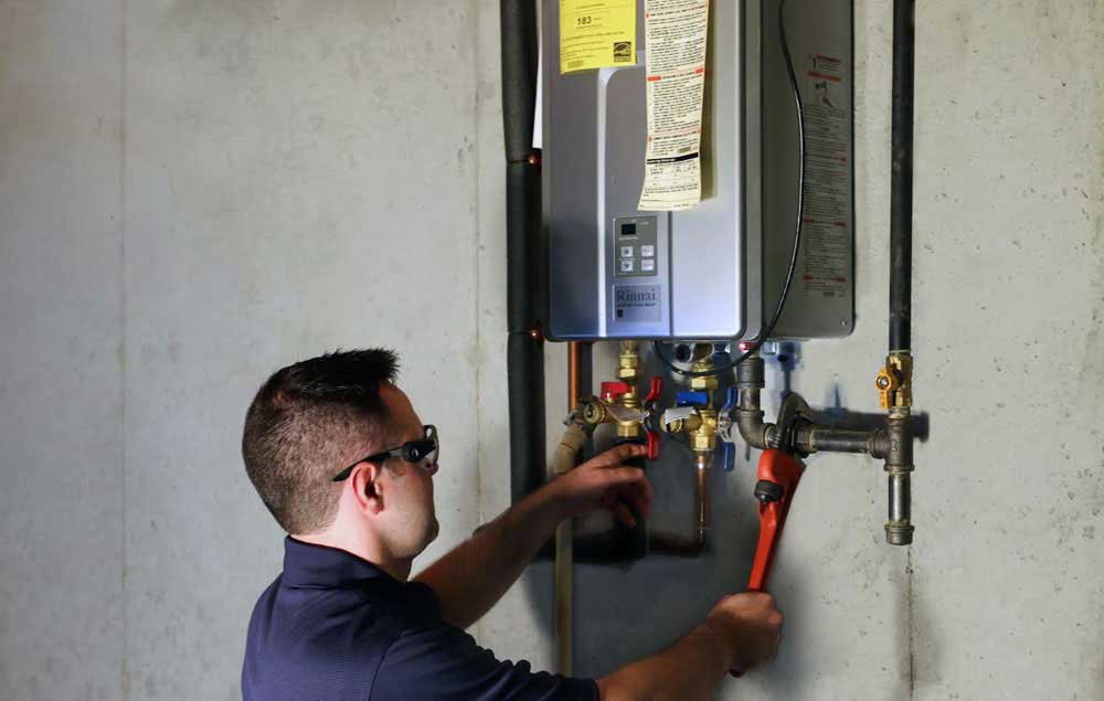 Technician installing a tankless water heater, adjusting valves and connections, in a residential setting.