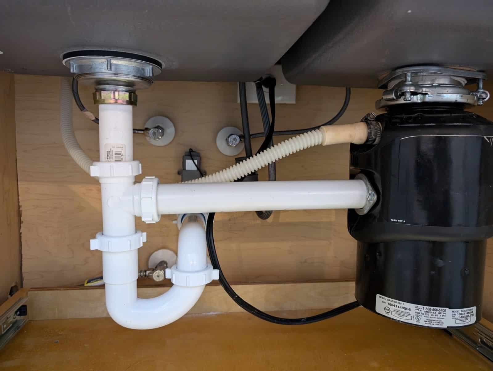 Under-sink plumbing setup featuring a garbage disposal unit, PVC pipes, and plumbing connections, relevant to Plumbing Outfitters' services in Cedar Park.
