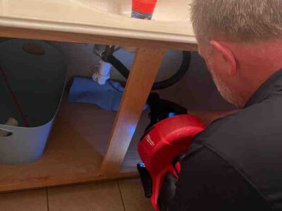 Plumber using a drain cleaning tool under a sink, addressing plumbing issues related to gurgling noises and slow drainage.