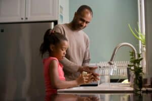 family filling glasses with filtered tap water at home kitchen sink